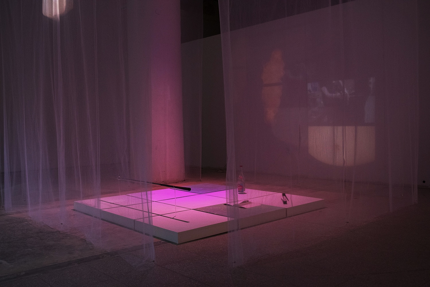 The Teahouse is an installation with found objects, glass, and video projections. The piece is approximately the size of a three feet cube. It was set up in the City Art Space in downtown Rochester. On the site, the installation was surrounded by four layers of white sheers hanging down from the ceiling. On the white sheer fabric, a short film was projected. With the translucency of this material, the film projects through one fabric to the other side, casting a blurred image of the video. In between each fabric, there was a gap that allowed people to walk into the installation. Inside the white cube, there were nine white low pedestals. Eight of them had objects or words on them, and only the one in the middle remained empty. These were the objects that were shown in the video.