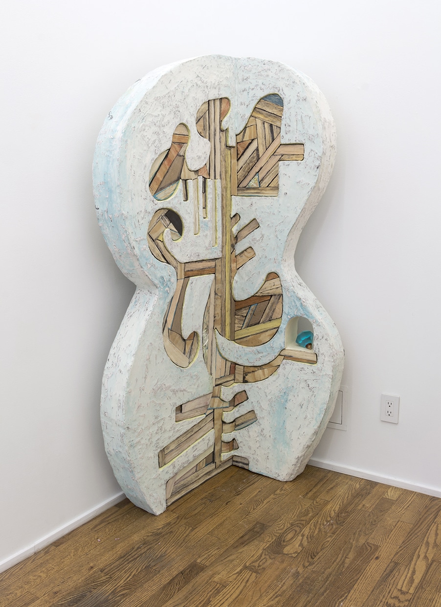 This 6-7’ tall sculpture is in the shape of a right angle, and is positioned in a right angled corner of an architectural space, hovering about 5” in front of the walls. It is approximately 5” thick on either side before it turns 90 degrees, opening up like a book parallel to the walls. It is a large rounded stele form, with undulating curves toward the center of the 5” wide sides, resemblant of an instrument. The majority of its surface is a white, baby blue, and graphite stone-like texture. Toward the center of the form, particularly where it folds into a right angle, are fragmented pieces of wood which are arranged like a mosaic embedded into the stone like structure. The wood is adhered in several different directions, and while the natural character of the wood is retained, some pieces are painted black, washed glue, or tinted yellow. The overall frame/footprint of the embedded wood mosaic is an extremely undulating, curvilinear, cartoonishly organic shape. This overall shape moves from incredibly bulbous French curves, to sudden vertical lines, to organ like protrutions from a central form. There is one negative space cut out from the right side of the stone-like form, a 5" archway, that sits atop two horizontal fragments of wood. Sitting at the base of this archway is a translucent blue cast resin diamond, sitting on one of its side facets, approximately 3.5” in height and diameter.