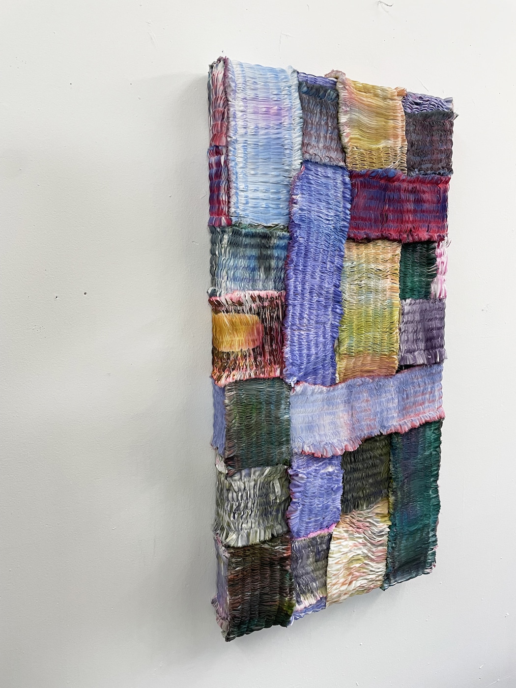A painting made up up pleated fabric in a variety of colours.