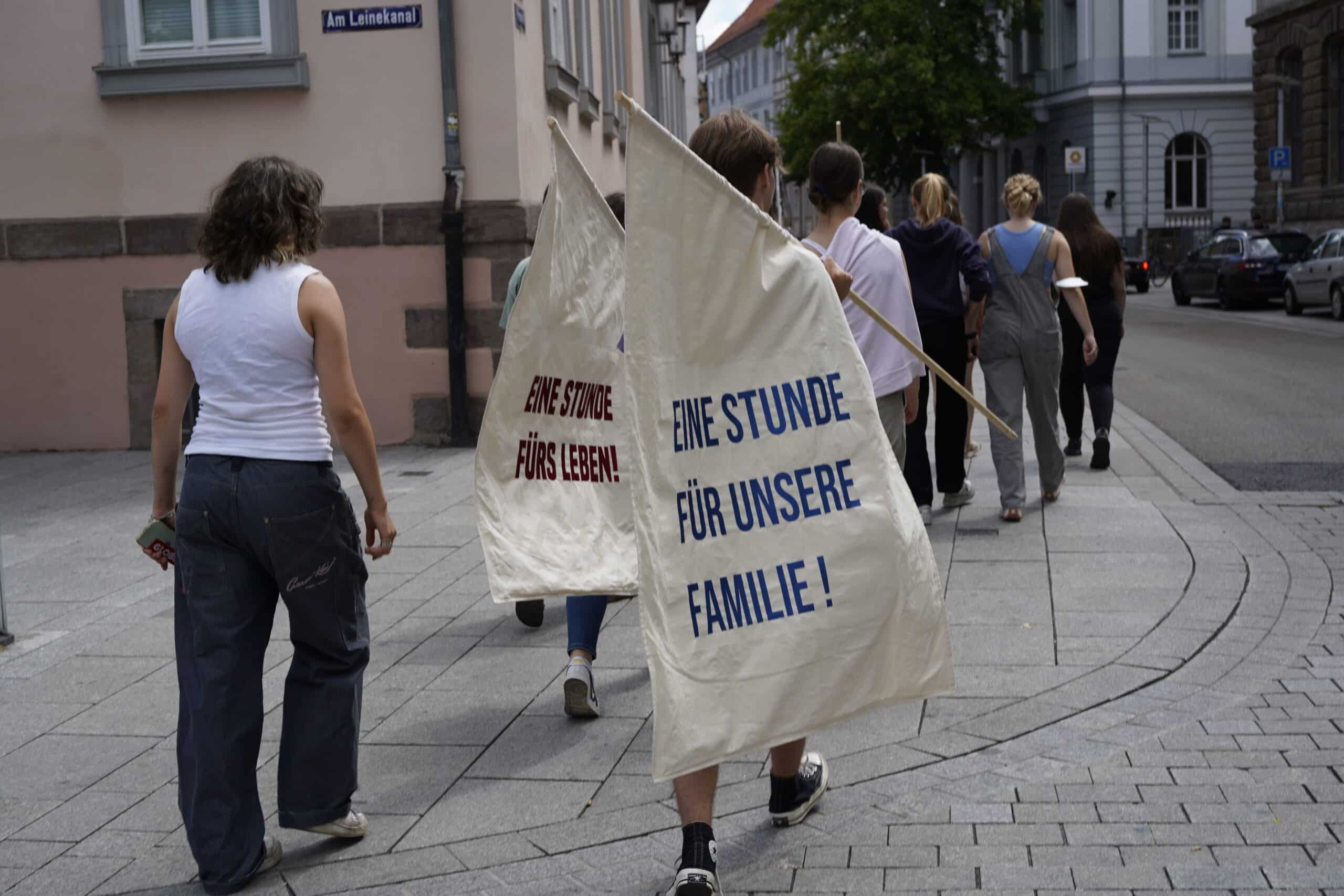 Several people carrying flags through the streets, showing slogans from the textile strikes of the 19th century in Germany.